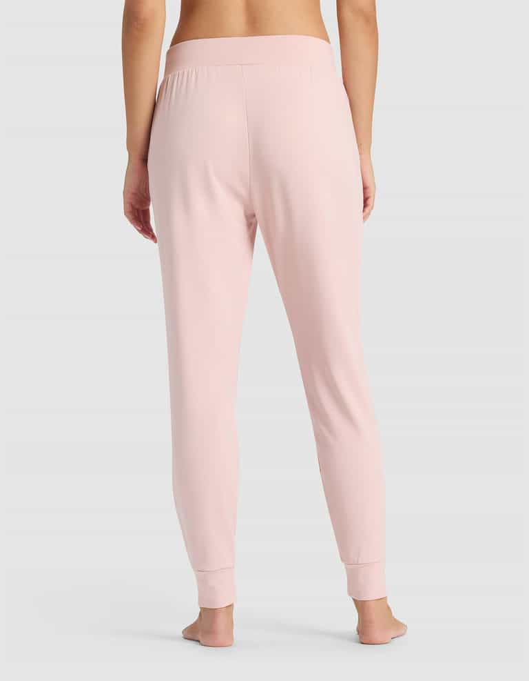 A person stands barefoot facing away, wearing Cozy Earth's Women's Brushed Bamboo Jogger Pant in light pink with an elastic waistband and fitted cuffs, set against a plain light gray background.|Color:Dusty Rose