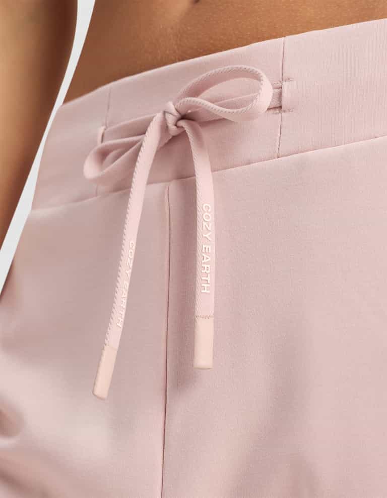 Close-up of Women's Brushed Bamboo Jogger Pant by Cozy Earth in pale pink, featuring a soft, comfortable fabric and a drawstring waistband tied in a bow with "COZY EARTH" printed in white.|Color:Dusty Rose