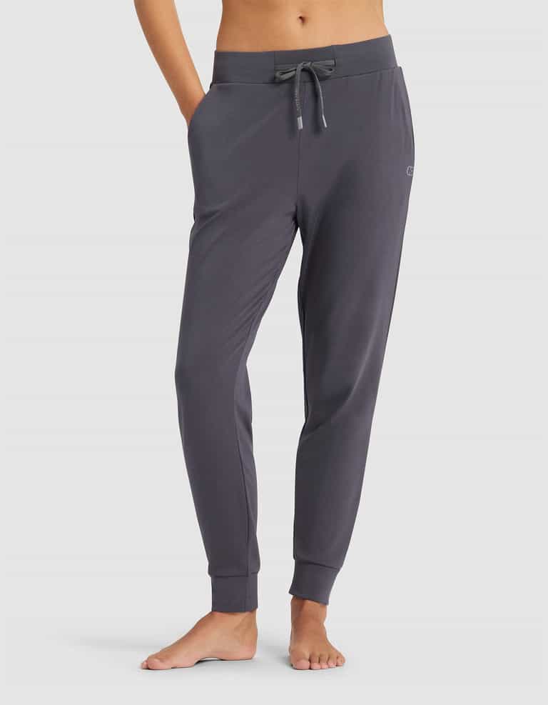 A person models Cozy Earth's Women's Brushed Bamboo Jogger Pant in dark gray, featuring a drawstring waist and pockets, standing barefoot against a plain light background. Upper body is not shown.|Color:Graphite