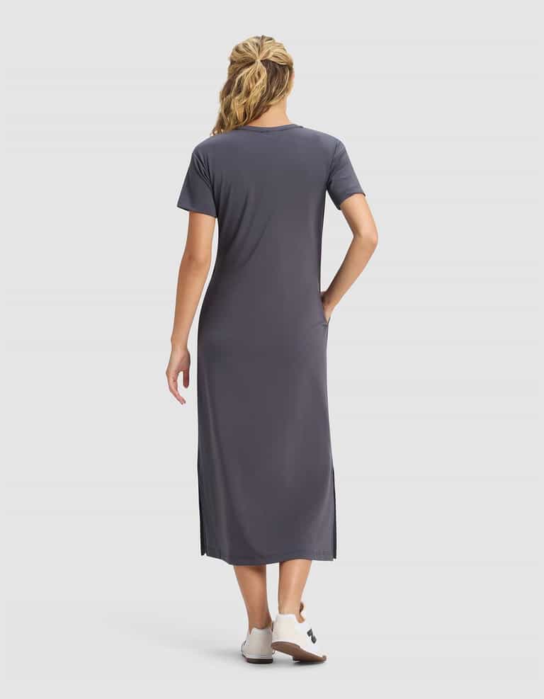 A woman with wavy blonde hair wears a Cozy Earth Women's Brushed Bamboo Midi Dress in gray and white shoes, standing with her back to the camera against a plain light background.|Color:Graphite