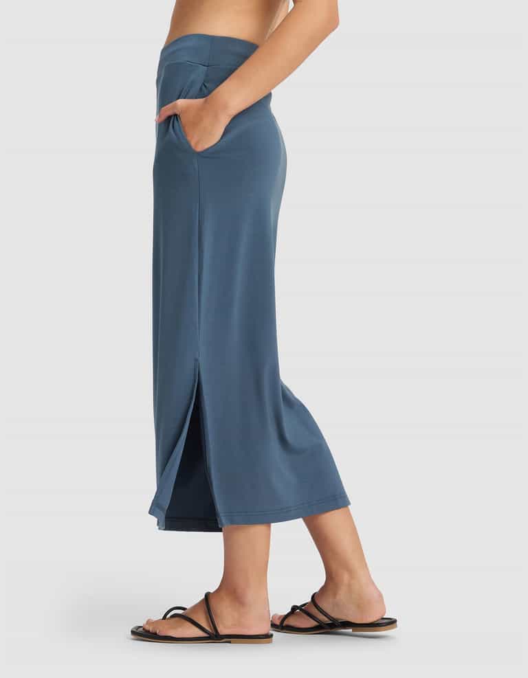 A woman wears the Cozy Earth Women's Brushed Bamboo Midi Skirt, standing sideways with one hand in her pocket against a plain light background.|Color:Dawn