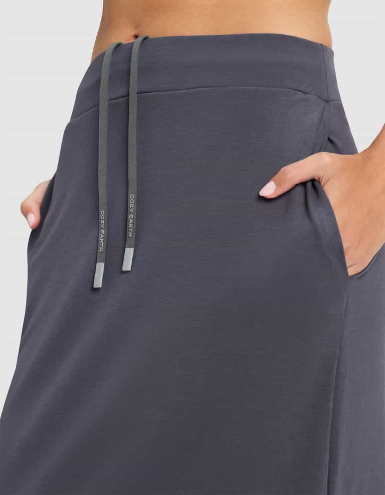 A woman wearing the Cozy Earth Women's Brushed Bamboo Midi Skirt in dark gray, featuring a high waist, side pockets, and a drawstring waistband with two drawstrings hanging down. |Color:Graphite