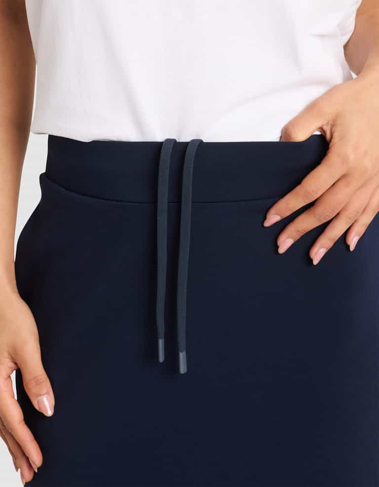 A person wears the Cozy Earth Women's Brushed Bamboo Midi Skirt in navy blue, featuring a drawstring waistband, paired with a white shirt; one hand rests on the waistband while the other is by their side. |Color:Navy