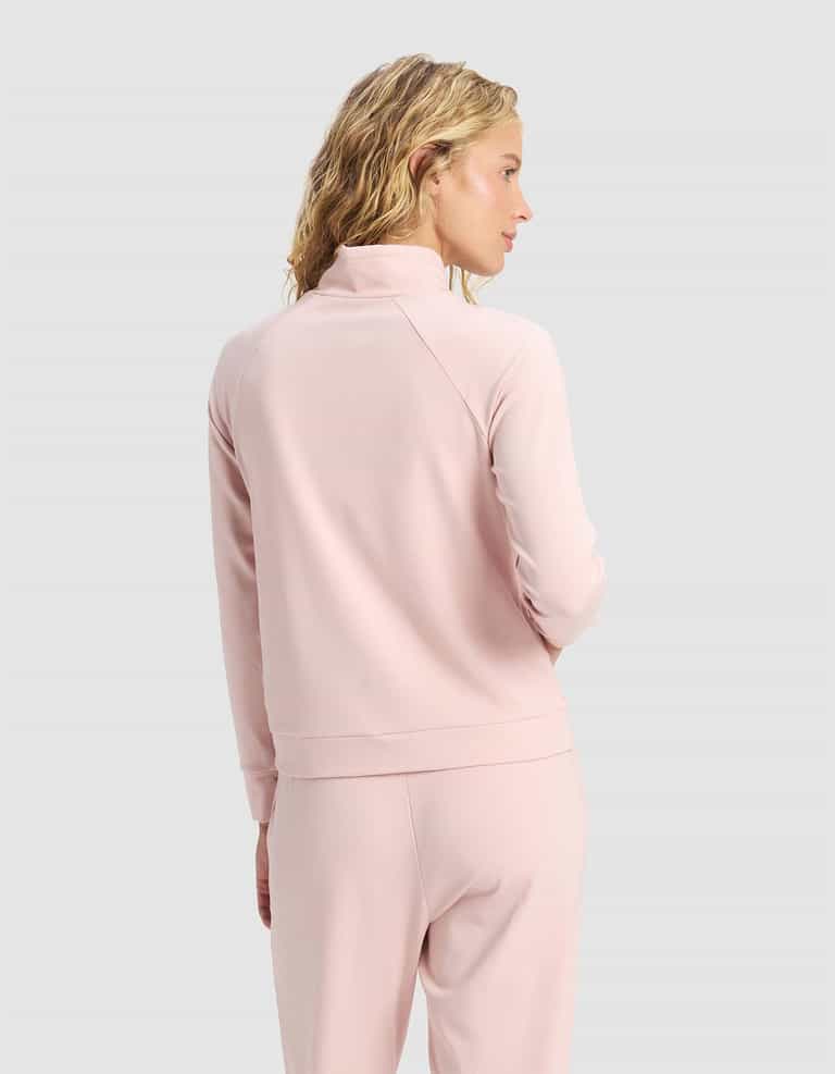 A woman with wavy blonde hair wears the Cozy Earth Women's Brushed Bamboo Mock Neck in light pink, standing against a plain light gray background with her head turned slightly to the side.|Color:Dusty Rose