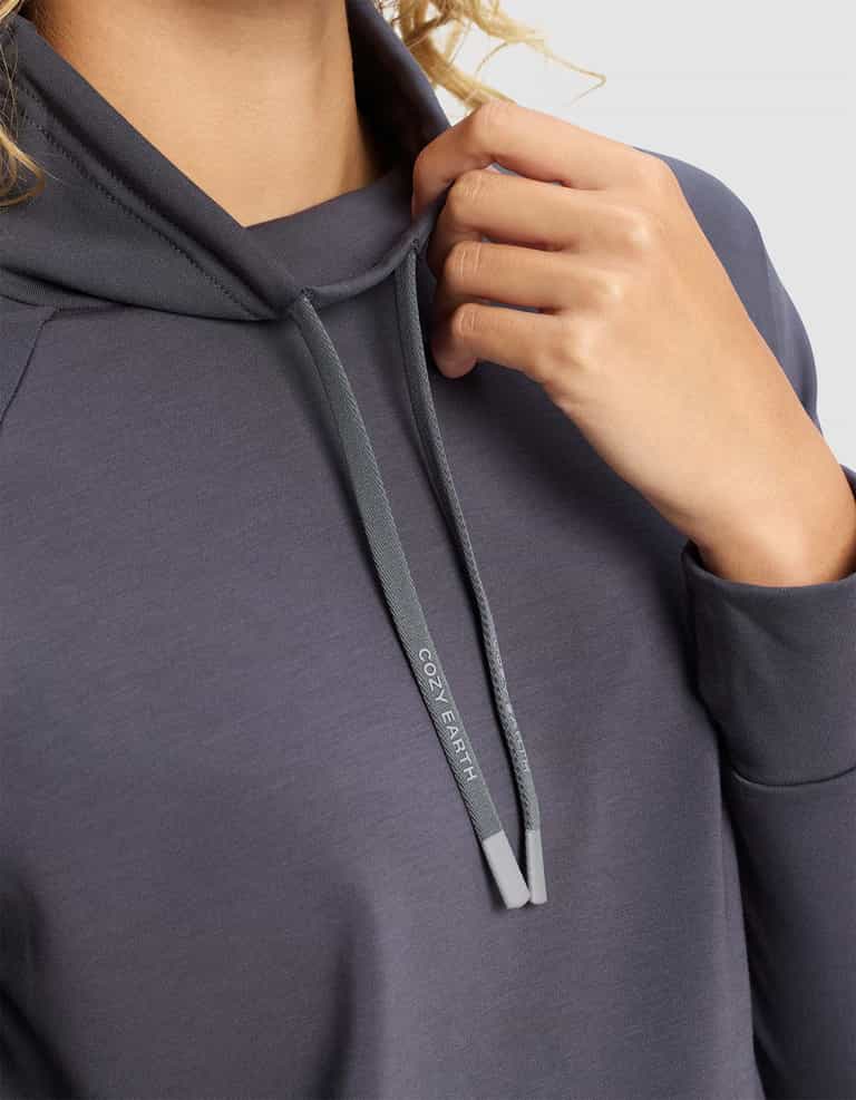 A person wearing the Cozy Earth Women's Brushed Bamboo Mock Neck holds a hood drawstring labeled “COZY EARTH,” with only their hand, part of their arm, neck, and the drawstring visible.|Color:Graphite