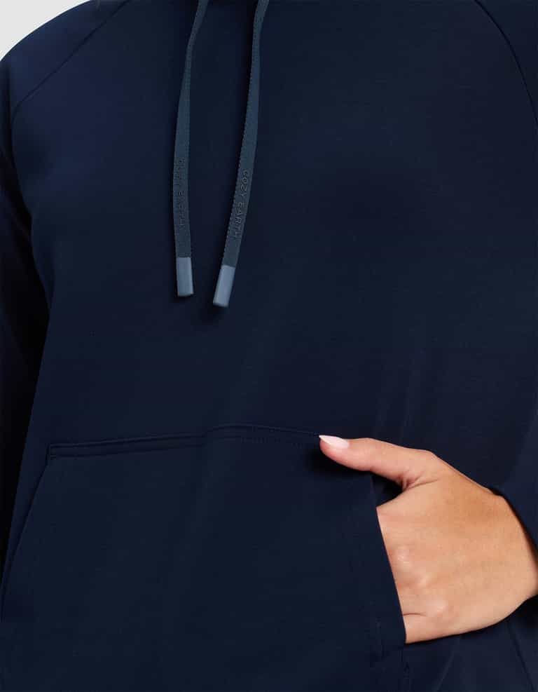Close-up of a person wearing the Cozy Earth Women's Brushed Bamboo Mock Neck in navy blue, featuring a front pocket, visible drawstrings near the neck, and their right hand partially inside the pocket.|Color:Navy