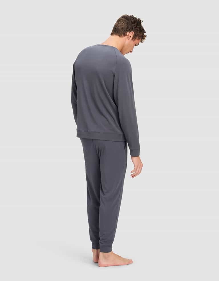 A man with short, tousled hair stands barefoot facing away, wearing the Cozy Earth Men's Brushed Bamboo Jogger Set in dark gray, against a plain light background.|Color:Graphite
