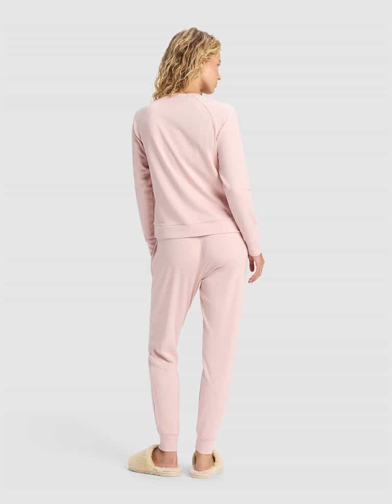 A woman with curly blonde hair faces away, wearing the Cozy Earth Women's Brushed Bamboo Jogger Set in light pink and beige fuzzy slippers, set against a plain light gray background.|Color:Dusty Rose