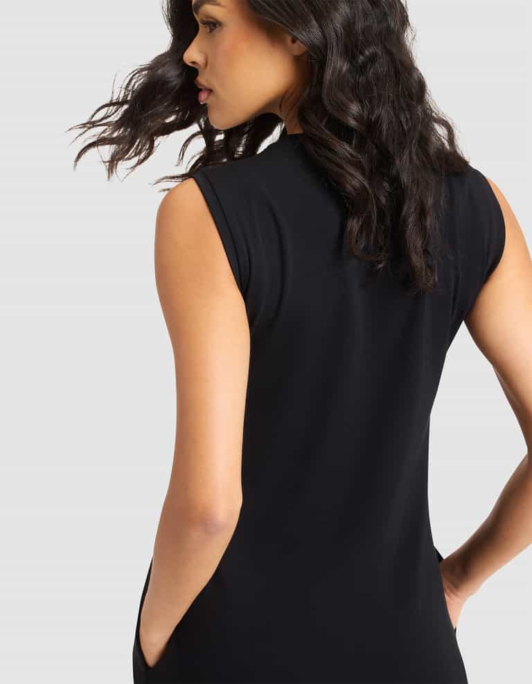 A woman with wavy dark hair models the Cozy Earth Women's Brushed Bamboo Sleeveless Midi Dress in black, standing against a light background with her back mostly to the camera and her head turned slightly to the side. |Color:Black