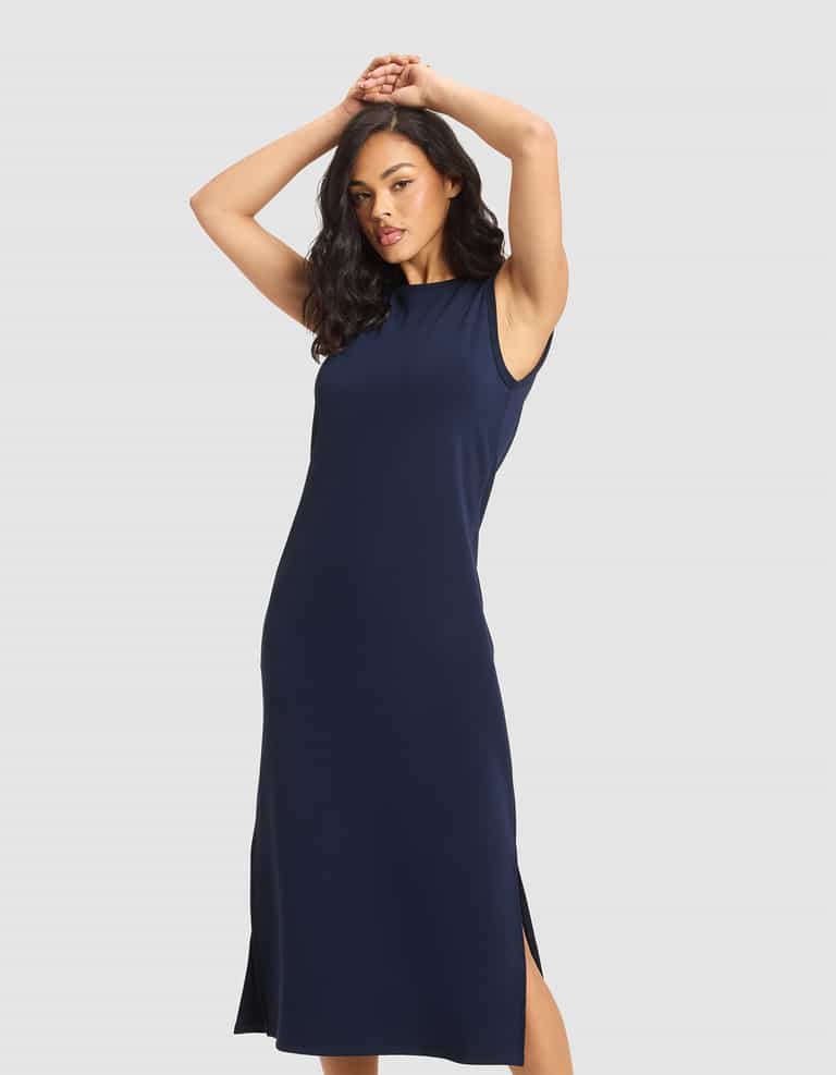A woman wears the Cozy Earth Women's Brushed Bamboo Sleeveless Midi Dress in navy, standing against a plain light background with her arms raised and hands clasped. |Color:Navy