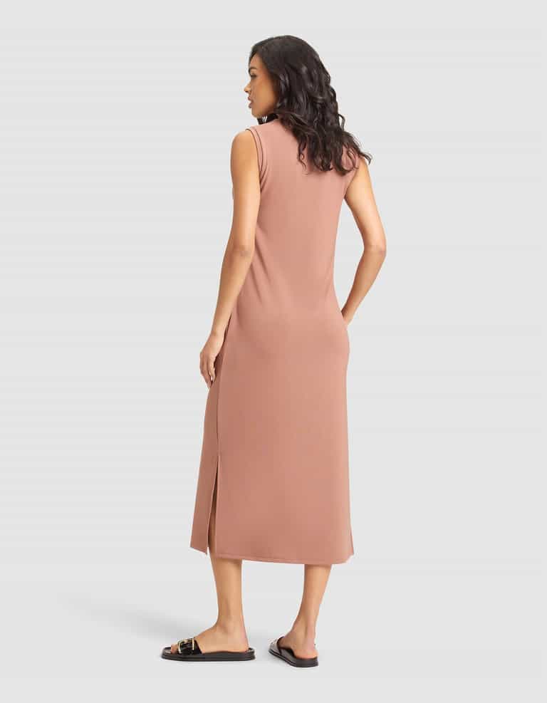 A woman with wavy dark hair, wearing black flat sandals and the Cozy Earth Women's Brushed Bamboo Sleeveless Midi Dress in rose, stands facing away against a plain light gray background. The knee-length dress features a side slit. |Color:Saddle