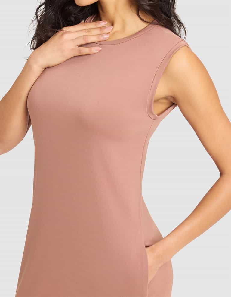 A woman models the Cozy Earth Women's Brushed Bamboo Sleeveless Midi Dress in light mauve, with one hand touching her collarbone and the other in a pocket; her face is not shown. |Color:Saddle