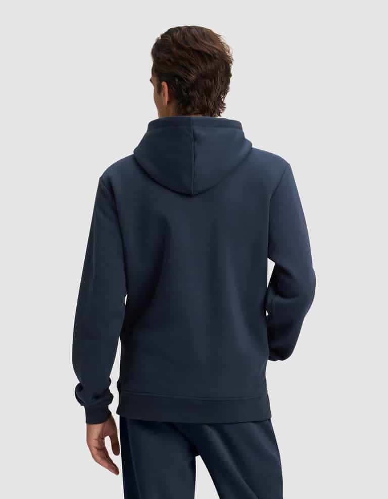 A man with short brown hair is seen from behind wearing Cozy Earth's Men's Cityscape 2.0 Hoodie in dark blue, paired with matching pants, set against a plain light gray background.|Color:Eclipse