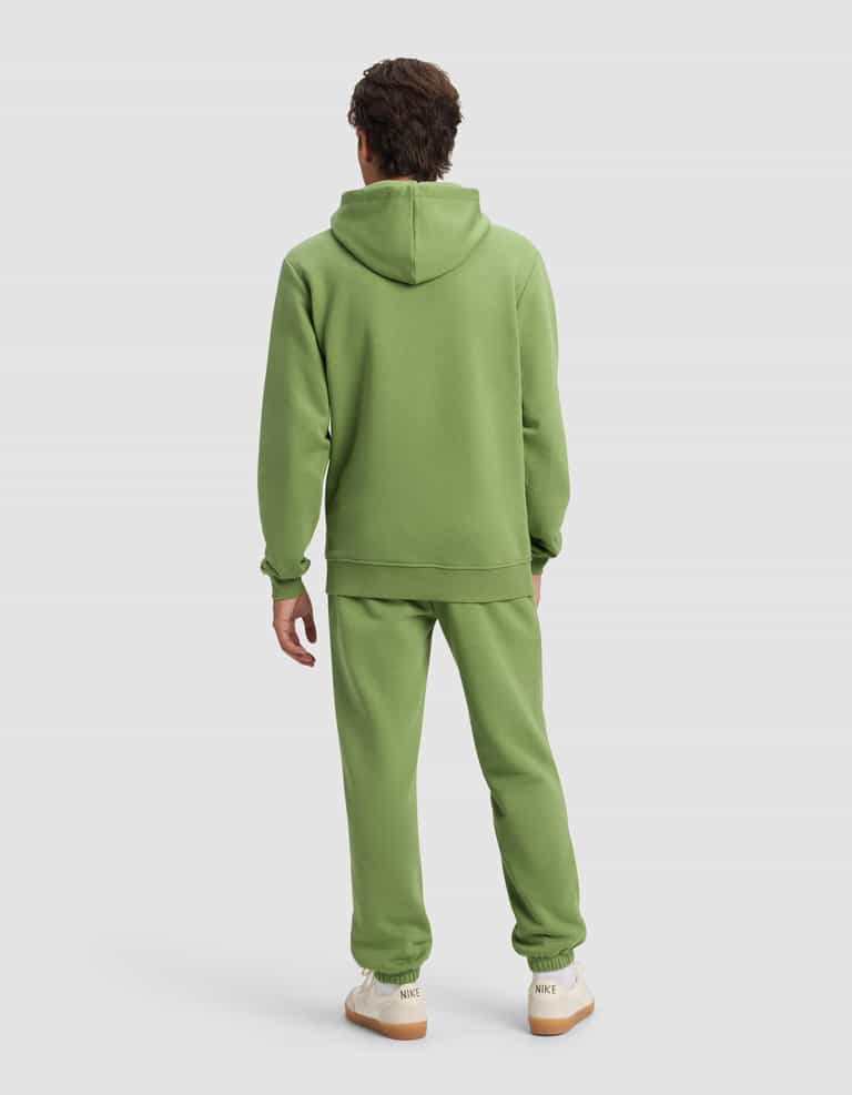 A person with short brown hair is standing and facing away, wearing Cozy Earth's Men's Cityscape 2.0 Hoodie & Sweatpant Set in light green and white sneakers with beige soles, against a plain light background.|Color:Clover