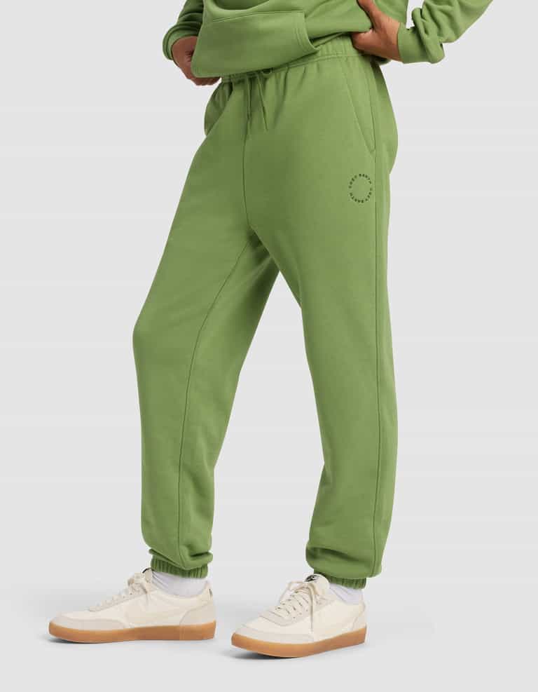 A person wearing Cozy Earth Men's Cityscape 2.0 Sweatpant in green with a matching sweatshirt, white socks, and beige sneakers stands hands on hips against a plain light background.|Color:Clover