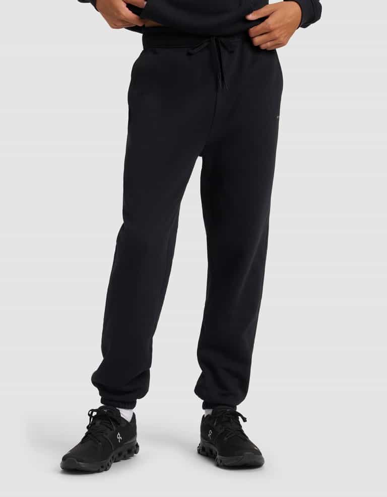 A person models the Cozy Earth Men's Cityscape 2.0 Sweatpant in black with matching sneakers, standing against a plain light gray background. Only the lower torso and legs are shown.|Color:Jet Black