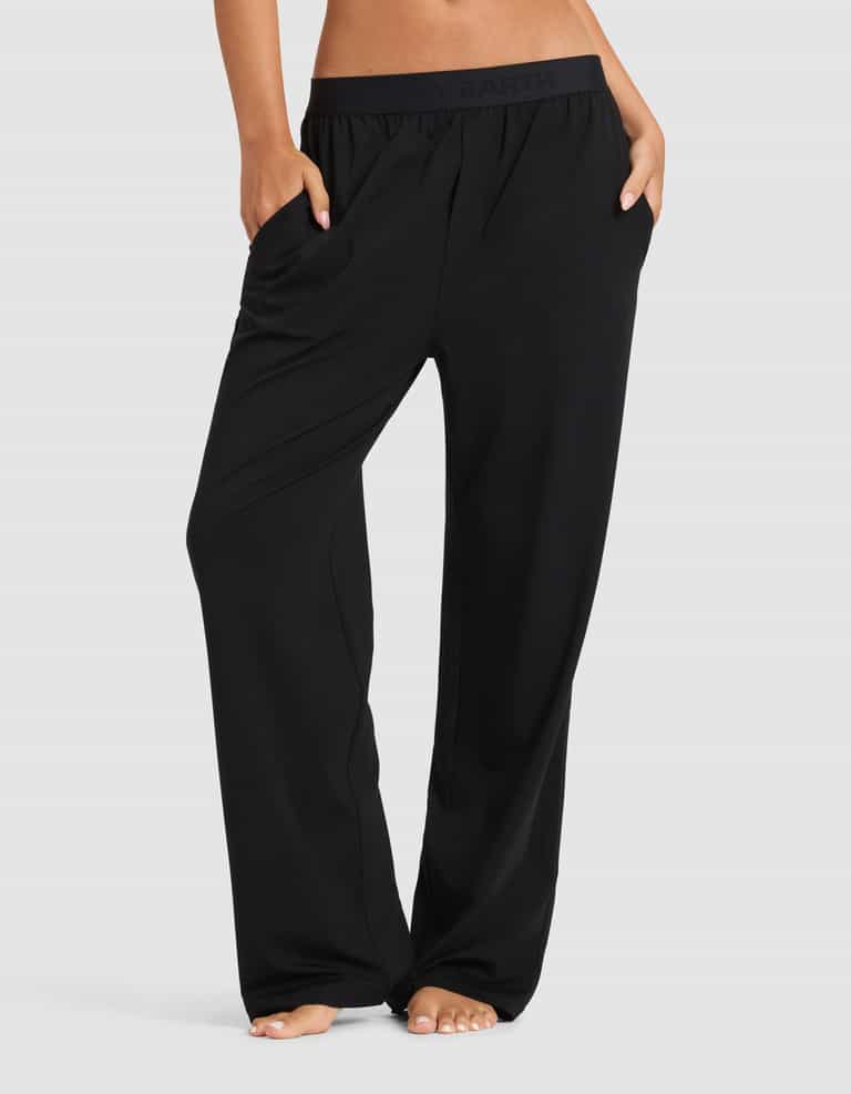 A woman stands barefoot with hands in her pockets, modeling Cozy Earth’s Women's First Layer Pajama Pant. Only the lower half of her body is visible against a plain light background.|Color:Jet Black