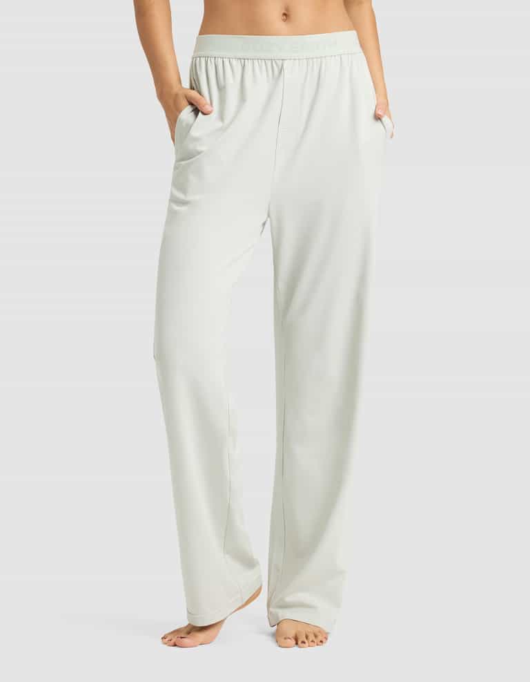 A person stands barefoot with hands in pockets, wearing Cozy Earth Women's First Layer Pajama Pant—light-colored, loose-fitting lounge pants featuring a relaxed fit and elastic waistband. Upper body is not visible.|Color:Laurel