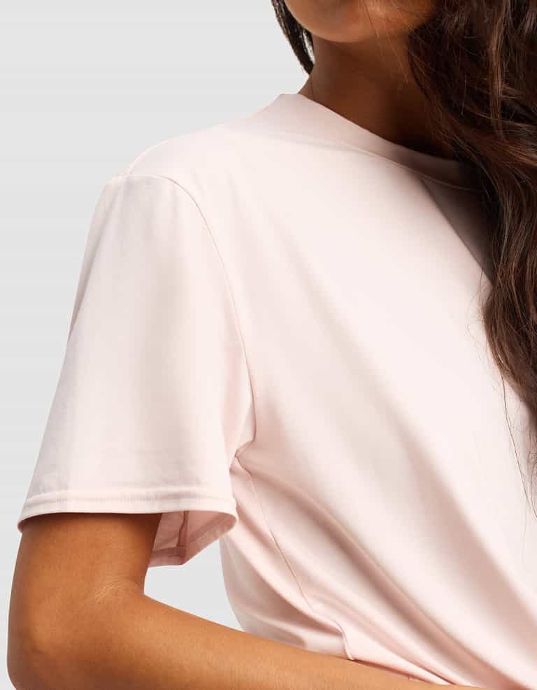 A woman with long, wavy brown hair models the Cozy Earth Women's First Layer Pajama Short Sleeve Tee in light pink, shown from shoulders to mid-torso against a plain gray background.|Color:Ballet