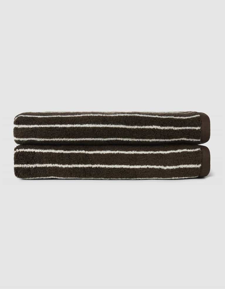 The Complete Striped Luxe Bath Bundle by Cozy Earth features two dark brown towels with thin, irregular white stripes, neatly rolled and stacked on a light gray background.|Color:Espresso Coconut Stripe