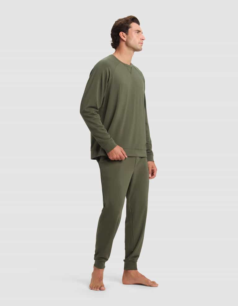 A man stands barefoot against a plain light background, wearing the Cozy Earth Men's Brushed Bamboo Jogger Set in olive green, featuring a long-sleeve top and matching pants. He faces sideways with a relaxed posture.|Color:Olive