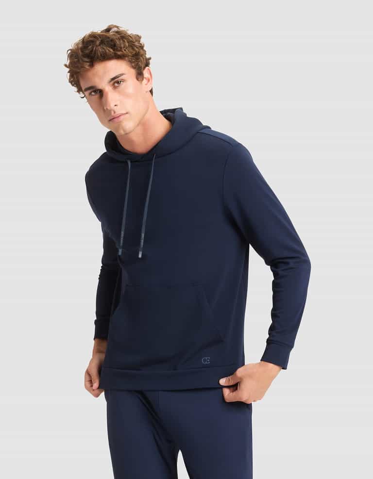 A young man wears the Cozy Earth Men's Brushed Bamboo Hoodie in navy blue, paired with matching pants, standing against a plain light gray background and looking at the camera with a neutral expression. |Color:Navy