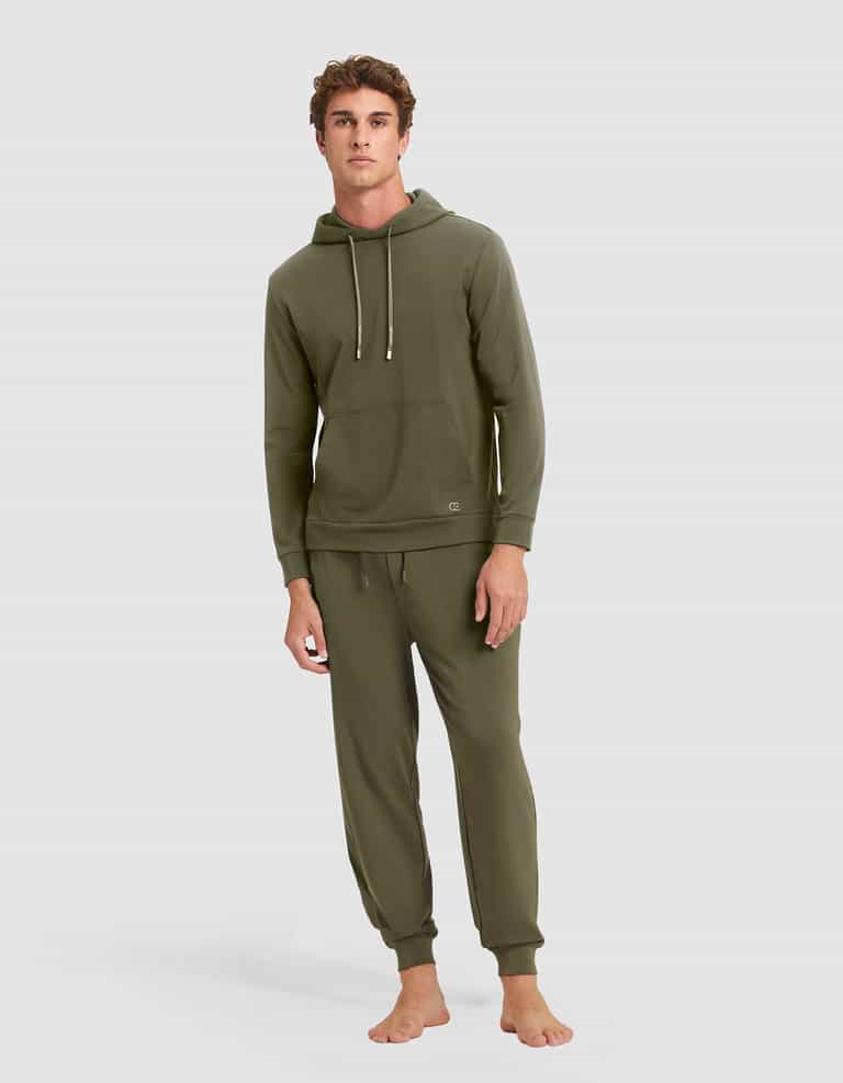 A young man stands barefoot against a gray background, wearing the Cozy Earth Men's Brushed Bamboo Hoodie & Jogger Set in olive green, featuring a hood with drawstrings and matching jogger pants. |Color:Olive