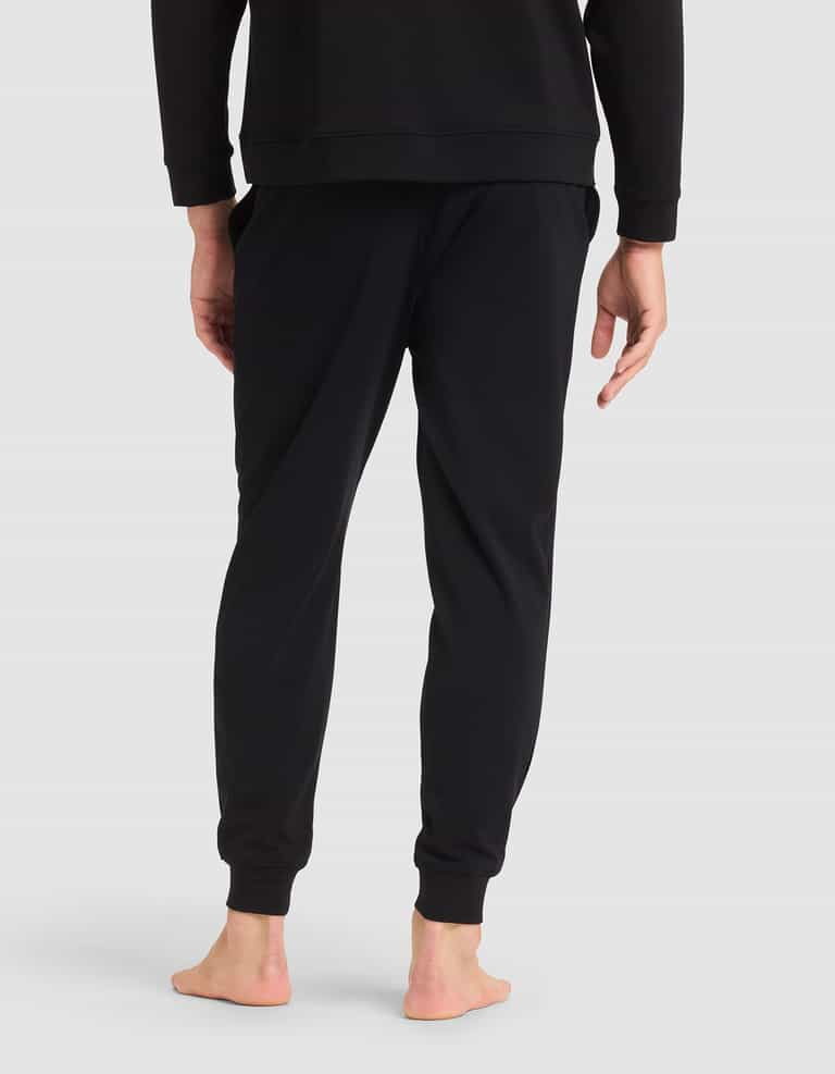 A person models Cozy Earth's Men's Brushed Bamboo Jogger Pant in black, paired with a matching sweatshirt, standing barefoot and facing away from the camera against a light gray background.|Color:Black
