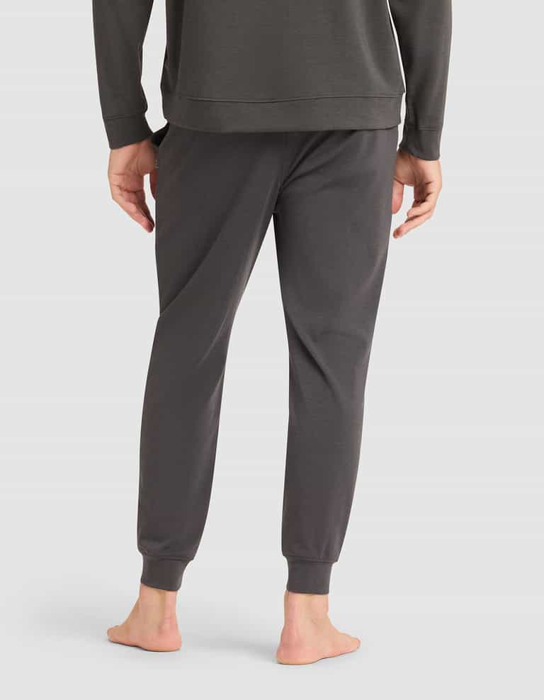 A person stands barefoot on a white background, shown from the back wearing Cozy Earth's Men's Brushed Bamboo Jogger Pant in dark gray paired with a matching long-sleeve top. |Color:Charcoal