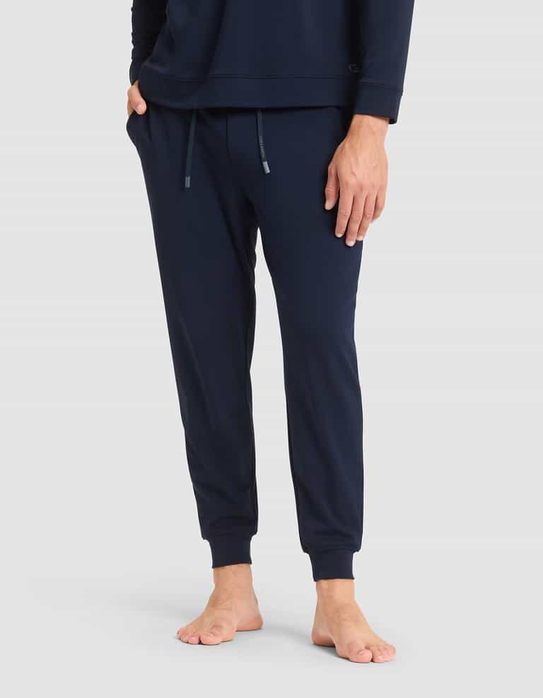 A person stands barefoot in Cozy Earth's Men's Brushed Bamboo Jogger Pant, featuring side pockets and an adjustable drawstring, paired with a matching navy top. One hand rests in a pocket while both arms are relaxed.