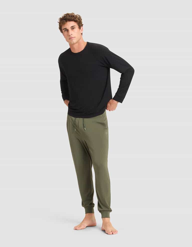 A man stands barefoot against a plain background, wearing a long-sleeve black shirt and Cozy Earth Men's Brushed Bamboo Jogger Pant in olive green, with his hands in his pockets. |Color:Olive