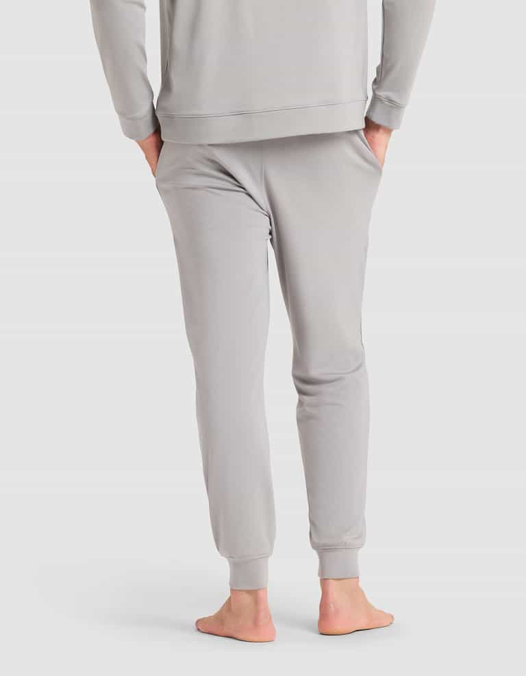 A barefoot man, seen from behind, wears Cozy Earth's Men's Brushed Bamboo Jogger in light gray with a matching long-sleeve top. |Color:Stone