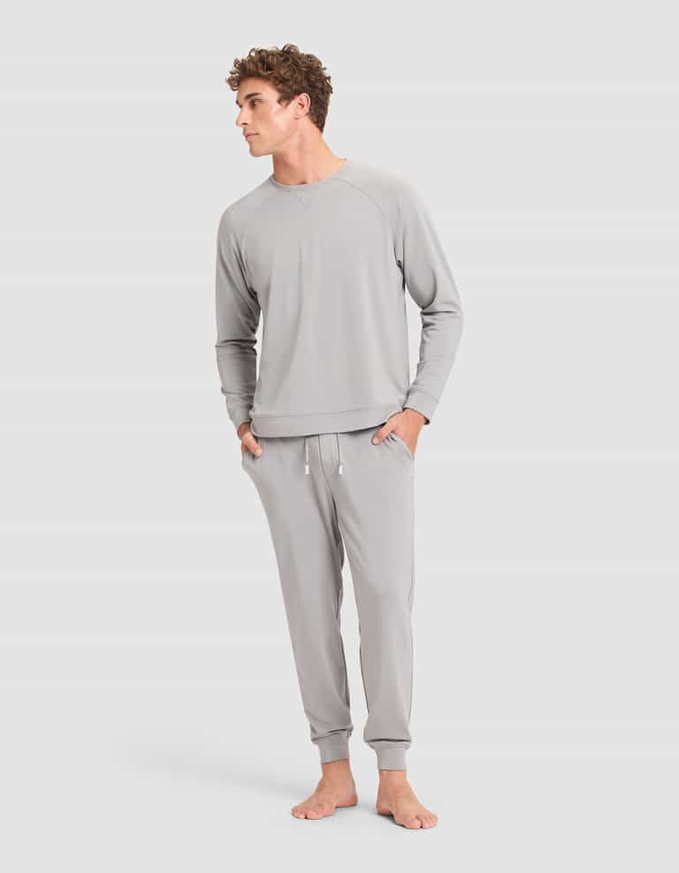 A man stands barefoot against a plain background, wearing the Cozy Earth Men's Brushed Bamboo Jogger in light gray, with his hands in his pockets and looking slightly to the side. |Color:Stone