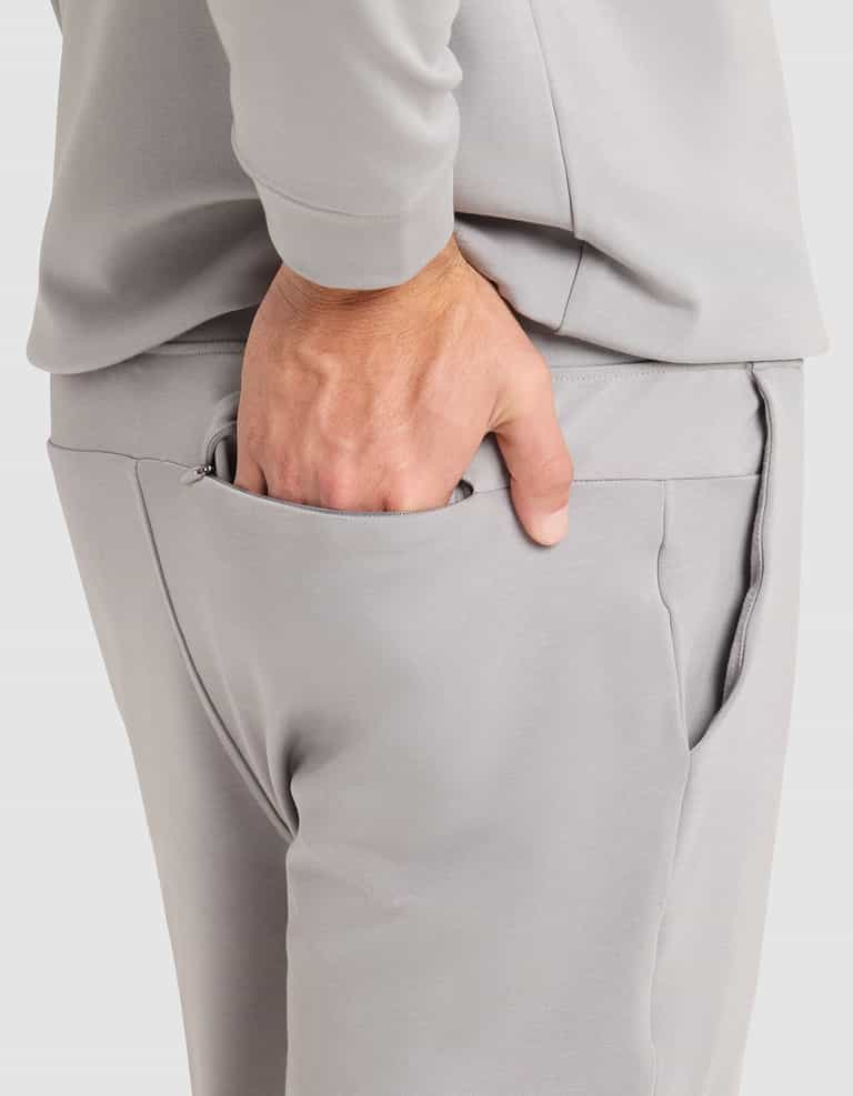 A person is shown from the waist down wearing Cozy Earth Men's Brushed Bamboo Jogger Pant in light gray, with a matching long-sleeve shirt and their right hand tucked into their pants pocket. |Color:Stone