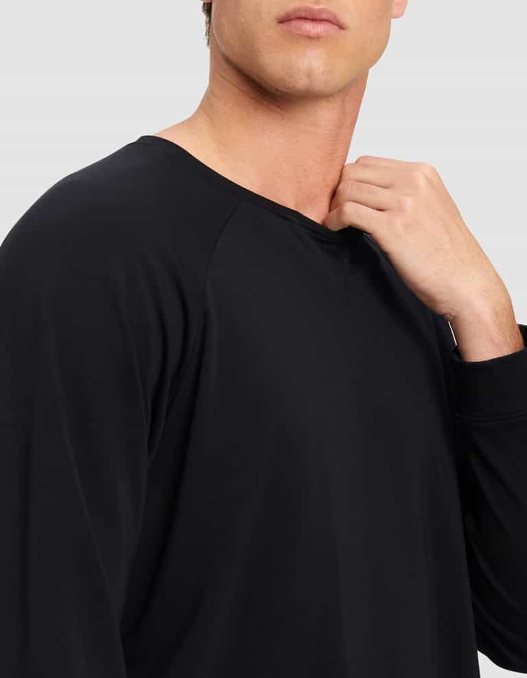 A man, his face partially visible, stands against a plain light background wearing the Cozy Earth Men's Brushed Bamboo Pullover Crew in black, with one hand touching the shirt's collar.|Color:Black