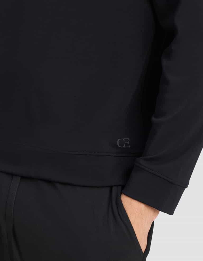 A person wearing the Cozy Earth Men's Brushed Bamboo Pullover Crew in black with one hand in their pocket, featuring a small "CE" logo near the waist.|Color:Black