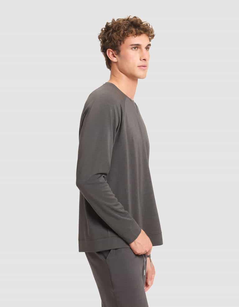 A young man with curly hair stands in profile against a plain light gray background, wearing a matching dark gray Men's Brushed Bamboo Pullover Crew by Cozy Earth. |Color:Charcoal