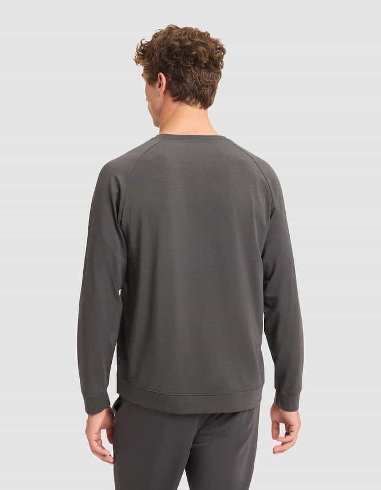 A man with short curly hair faces away from the camera, wearing a dark gray Cozy Earth Men's Brushed Bamboo Pullover Crew and matching pants against a plain light gray background. |Color:Charcoal