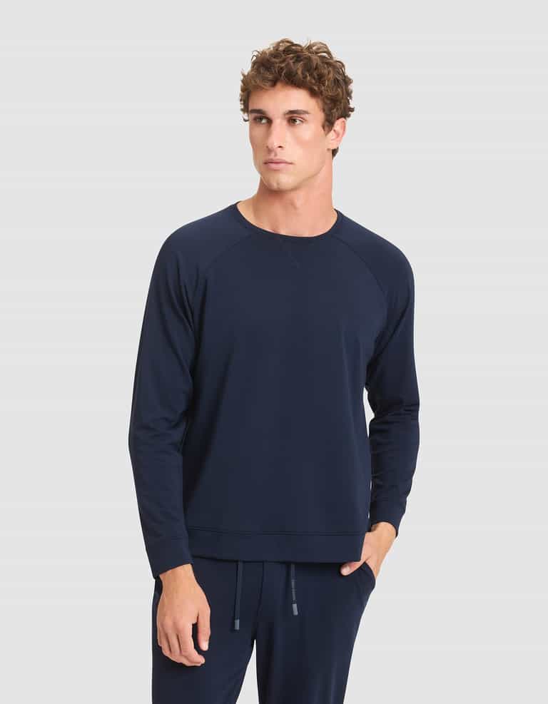 A man wearing the Cozy Earth Men's Brushed Bamboo Pullover Crew in navy blue stands against a light gray background, one hand in his pocket and a neutral expression on his face. |Color:Navy