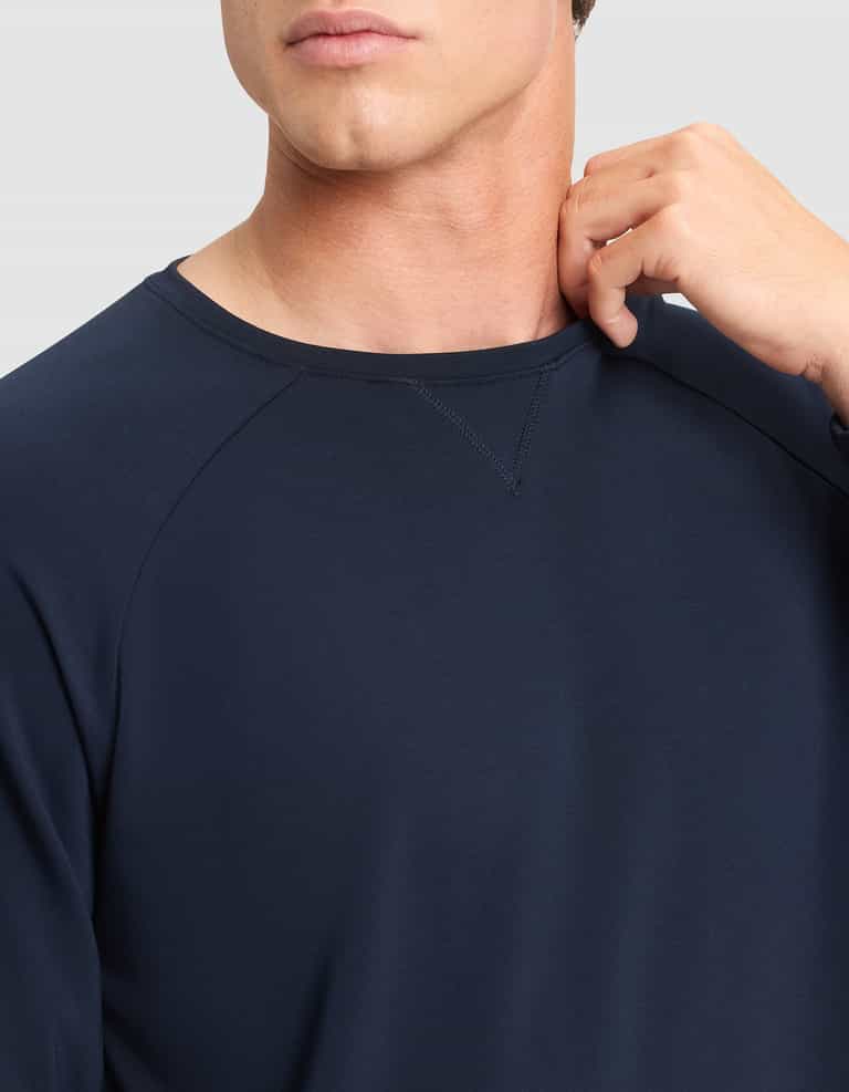 A man models the Cozy Earth Men's Brushed Bamboo Pullover Crew in navy blue, with only his lower face and upper torso visible as he stands against a light gray background, touching his neck with his right hand. |Color:Navy