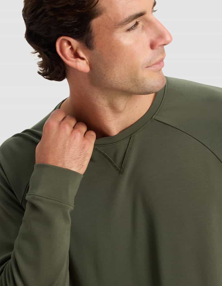 A man models the Cozy Earth Men's Brushed Bamboo Pullover Crew in olive green, touching the collar with his left hand against a plain light background.|Color:Olive