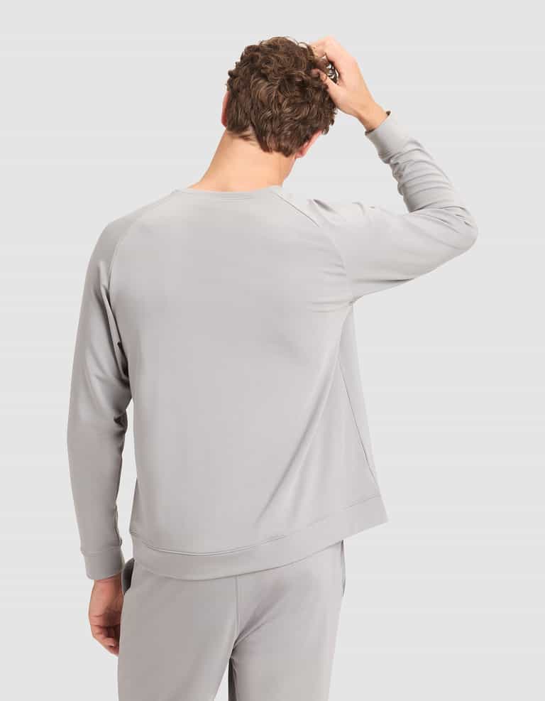 A person wearing the Cozy Earth Men’s Brushed Bamboo Pullover Crew in light gray stands with their back to the camera, right hand on their head, against a plain light background. |Color:Stone