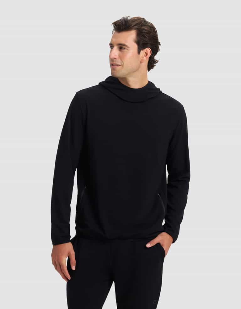 A man wears the Cozy Earth Men's Brushed Bamboo Recovery Hoodie and black pants, standing with one hand in his pocket and looking left against a plain light gray background. |Color:Black