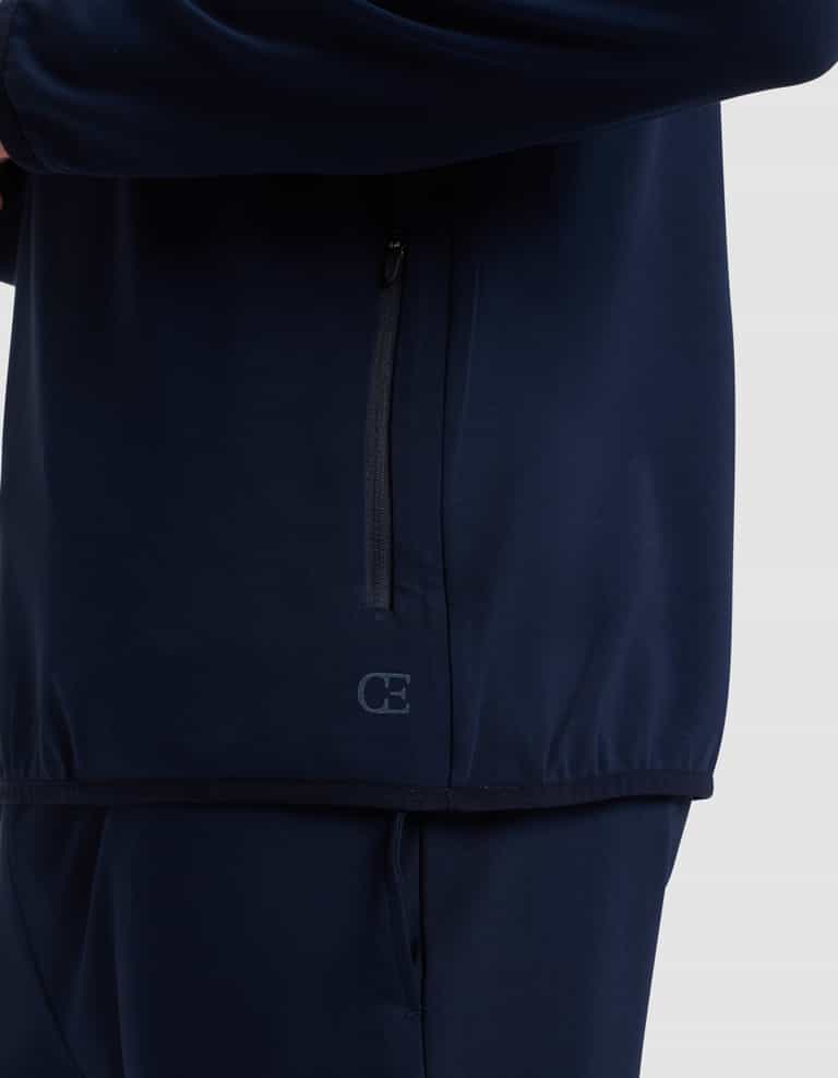 A close-up of a person wearing the Cozy Earth Men's Brushed Bamboo Recovery Hoodie in dark blue. The hoodie features a vertical zippered pocket and a small "CE" logo near the hem. Only the torso and upper legs are visible. |Color:Navy