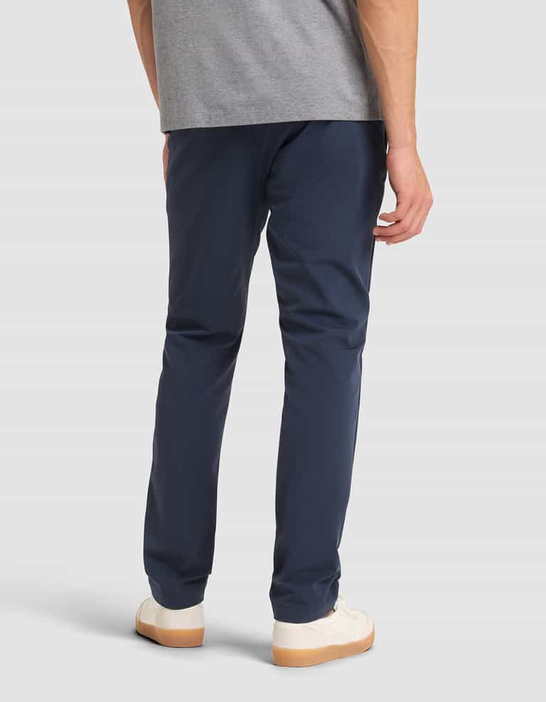 A person is shown from the back, standing against a plain background, wearing Cozy Earth’s Men's Everywhere Pant in navy blue, a gray t-shirt, and white sneakers with gum soles. |Color:Eclipse