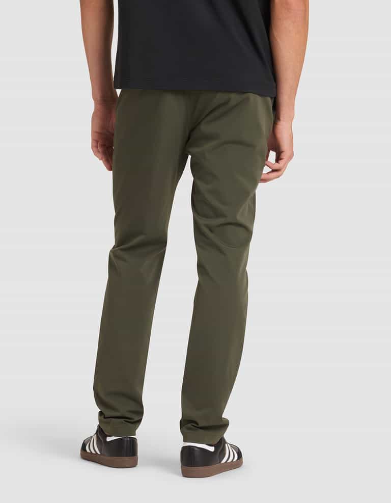 A person stands with their back to the camera, wearing Cozy Earth's Men's Everywhere Pant in olive green, a black shirt, and black sneakers with white stripes. |Color:Olive