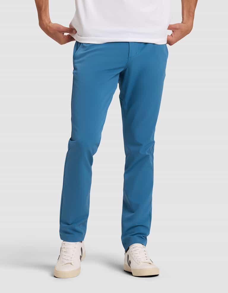 A person models Cozy Earth's Men's Everywhere Pant in bright blue with hands in pockets, paired with a white t-shirt and white sneakers, standing against a plain light gray background. The upper body is cropped from the image. |Color:Wave