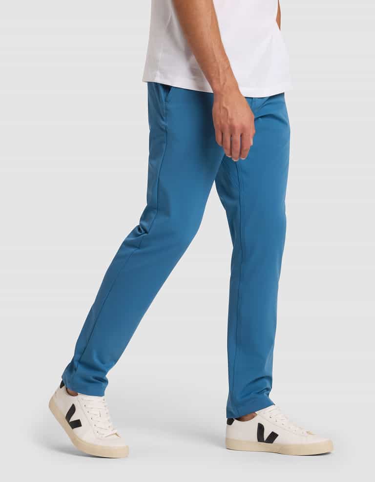 A person wearing Cozy Earth's Men's Everywhere Pant in teal-blue, a white t-shirt, and white sneakers with black "V" logos walks against a plain light gray background. |Color:Wave