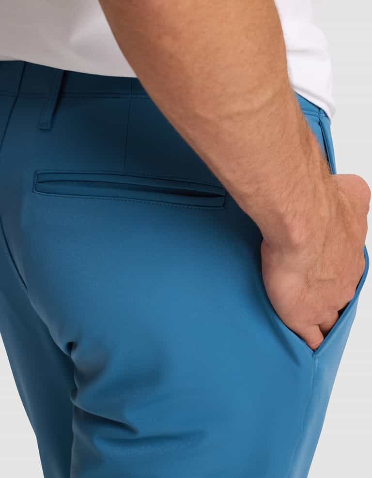 A man wearing Cozy Earth’s Men's Everywhere Pant in bright blue, shown from the waist down with his right hand in his pocket. The pants feature a back welt pocket and a white shirt is partially visible. |Color:Wave