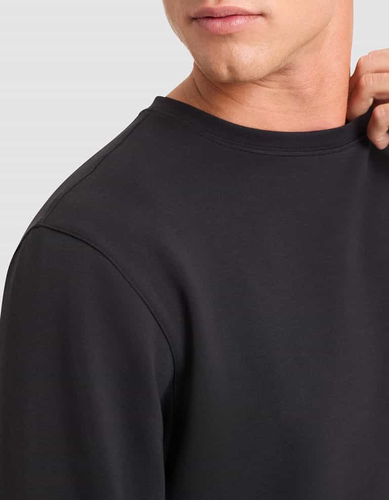 A close-up of a person wearing the Cozy Earth Men's StretchTech Crewneck in black, gently holding the collar. The image displays part of their face, neck, and upper torso. |Color:Jet Black